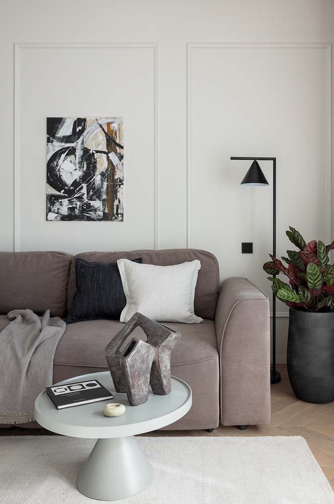 Decoração de sala minimalista com boiserie na parede, quadro estiloso e sofá de tecido cinza super confortável.