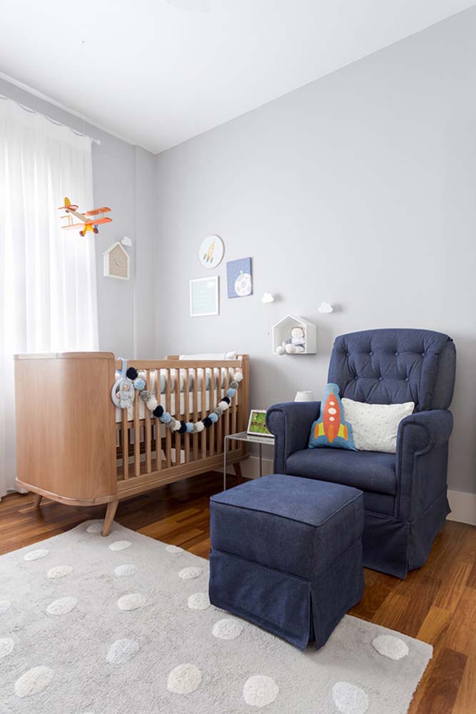 Poltrona azul marinho em quarto de bebê com pintura cinza.