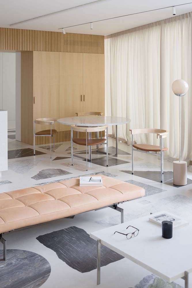 Sala moderna com mesa redonda com base metálica e pedra branca, acompanhando conjunto de cadeiras que também são ovais.