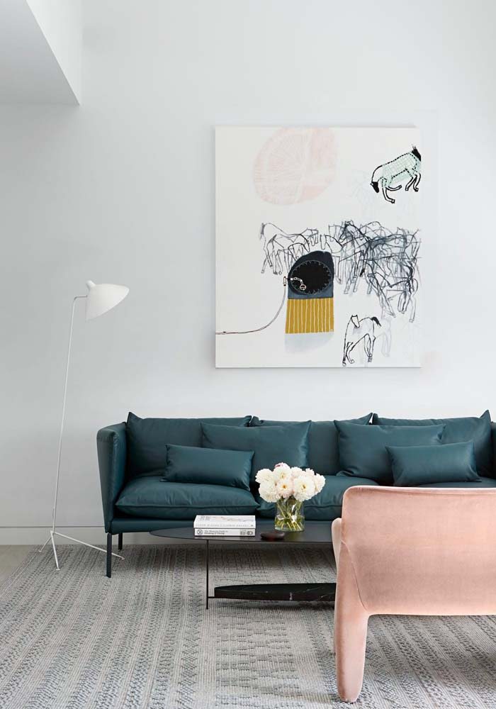 Sala minimalista com sofá verde escuro, poltrona rosa e quadro decorativo branco.