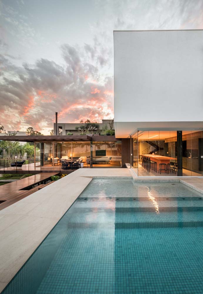A parede de vidro integra visualmente a área gourmet com a piscina