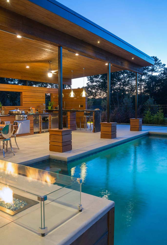 Área gourmet com piscina rústica. A madeira e a iluminação indireta é o charme desse projeto