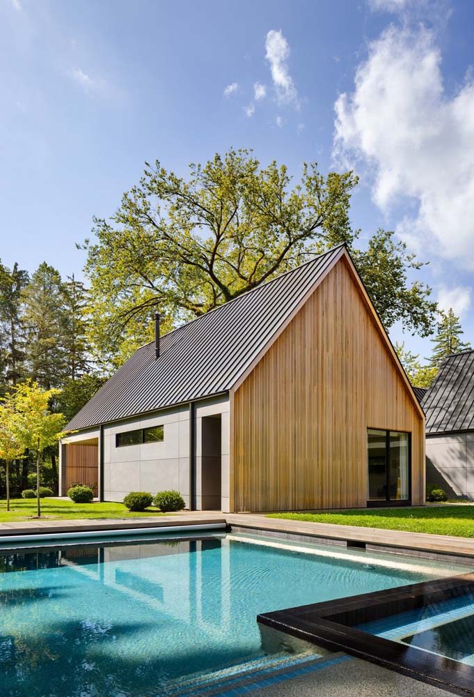 Modelo de casa imponente de madeira com telhado duas águas e área de piscina.