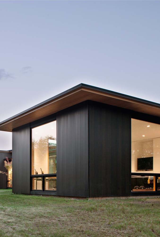 Casa de madeira térrea com telhado duas águas e amplas janelas de vidro.
