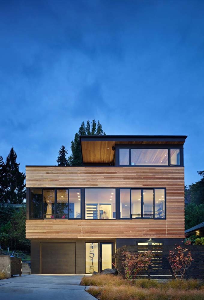Casa grande com revestimento externo de madeira e ampla presença dos vidros na fachada.