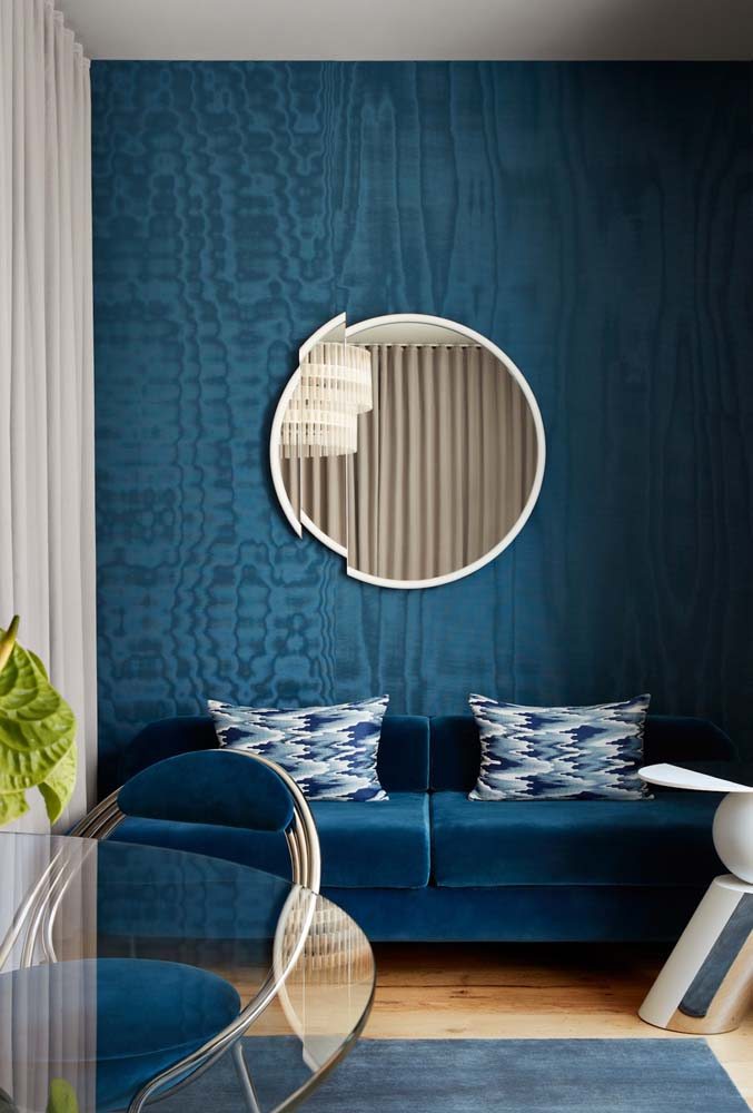 Sala de estar toda azul, dos móveis a parede com espelho decorativo redondo com moldura branca.