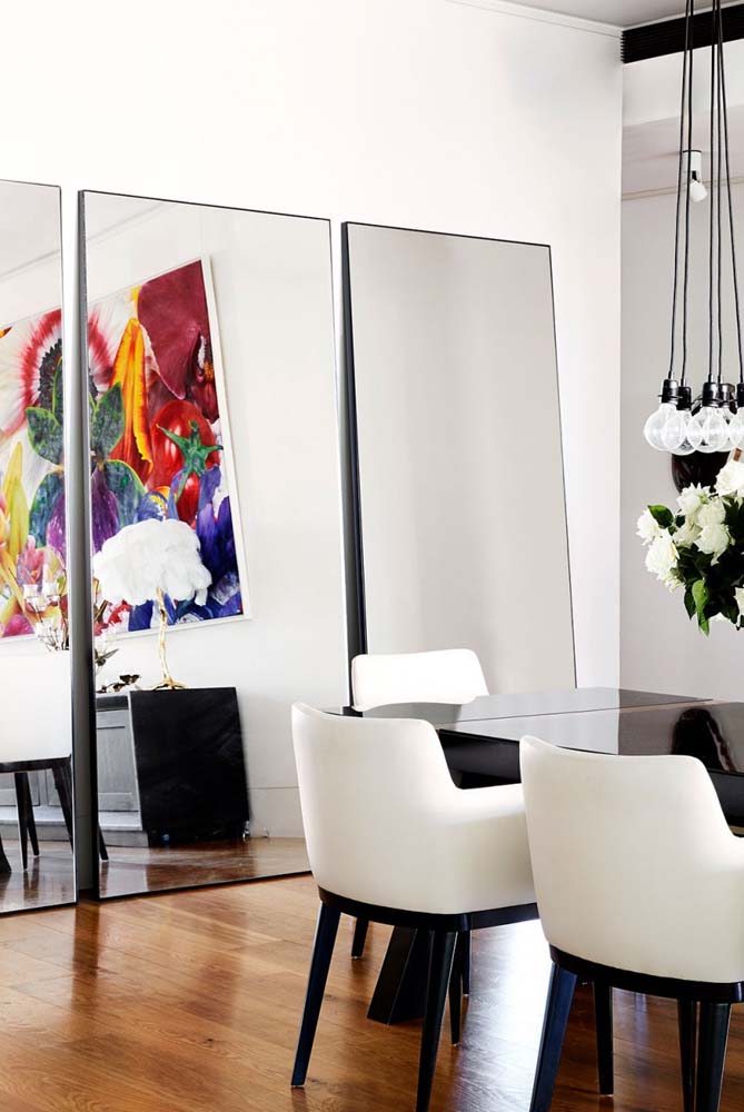 Sala de jantar com amplo espaço e trio de espelhos decorativos apoiados na parede.