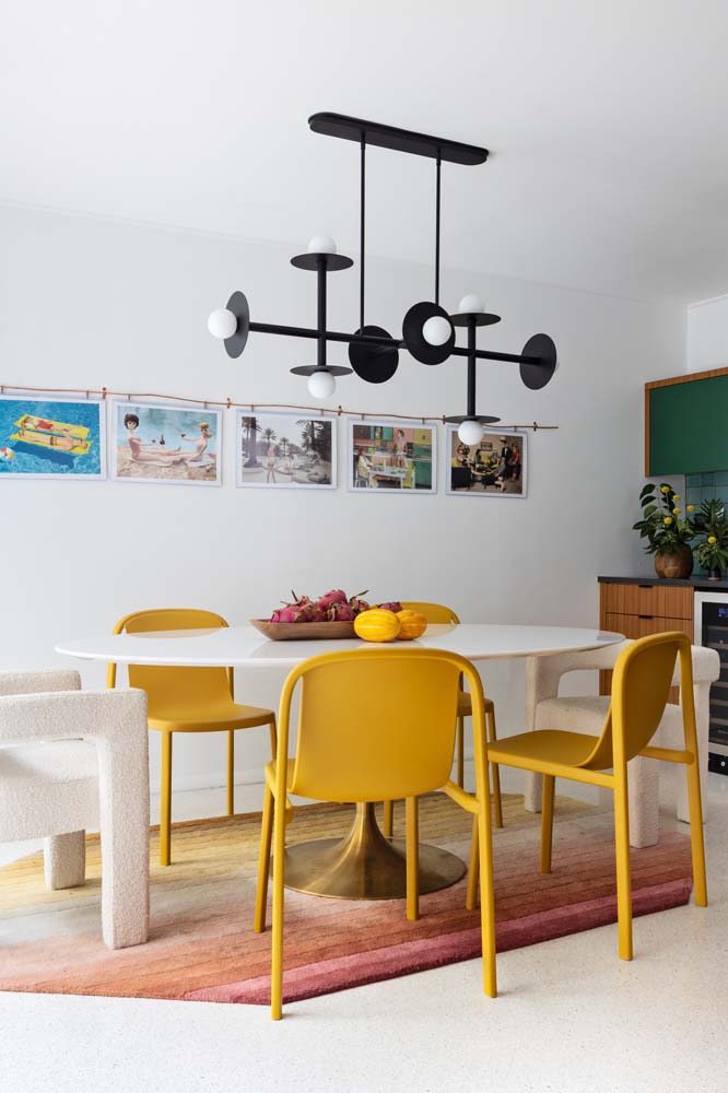 Modelo de mesa redonda branca com base metálica, cadeiras amarelas e lindo lustre diferente metálico na cor preta.