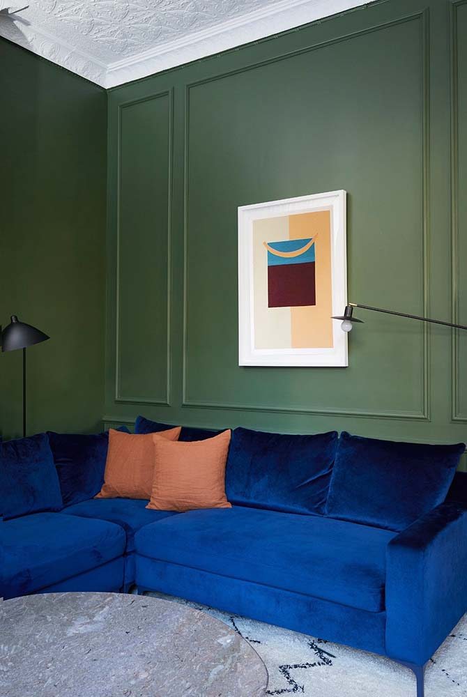Mix entre azul escuro do sofá com o verde da parede com boiserie na sala.