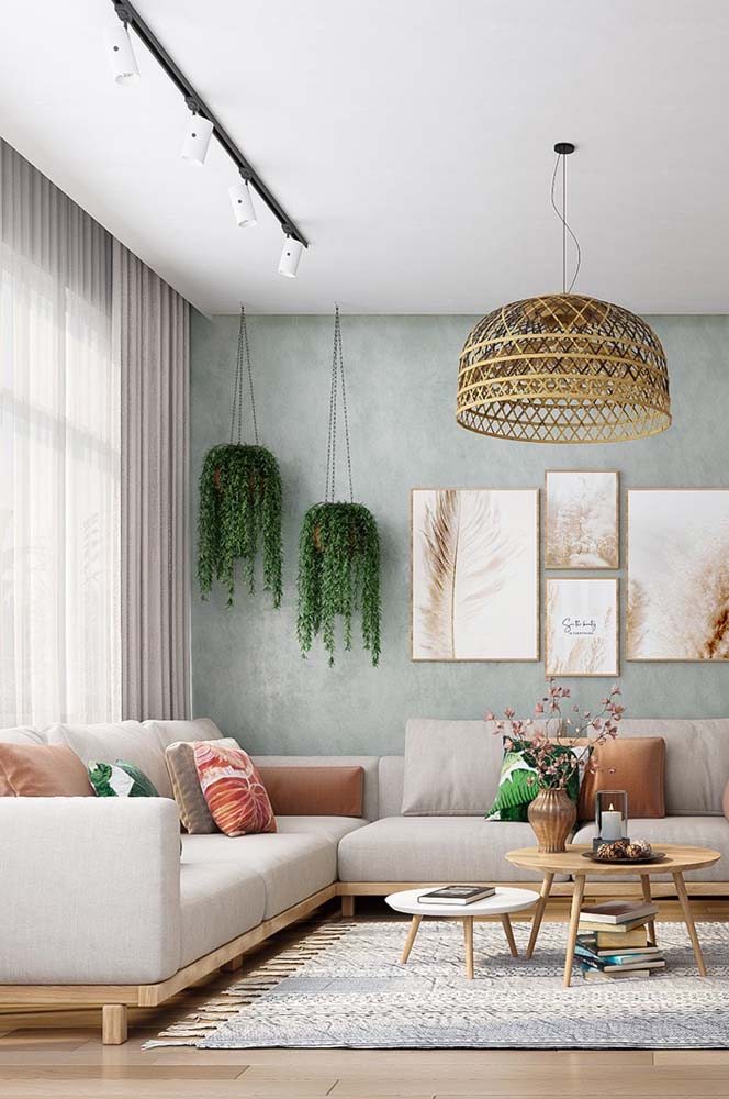 Sala charmosa com dupla de samambaias, papel de parede verde claro e sofá cinza de canto.