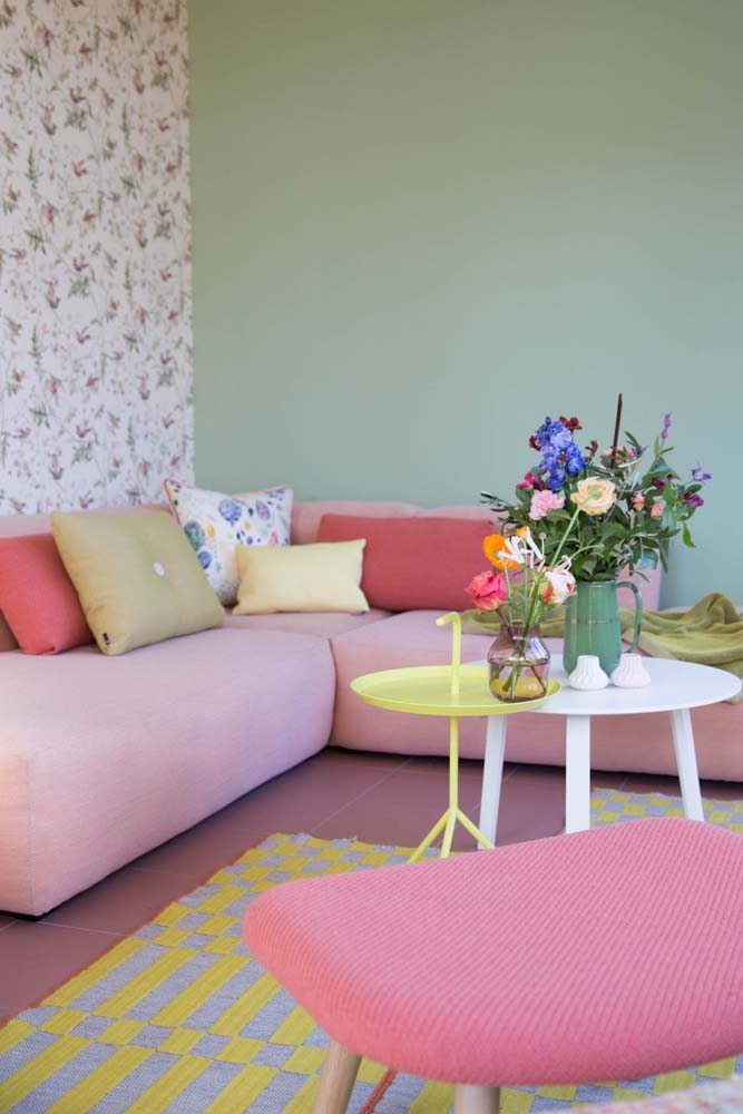 Cantinho da sala feminina com sofá de canto rosa e almofadas coloridas.