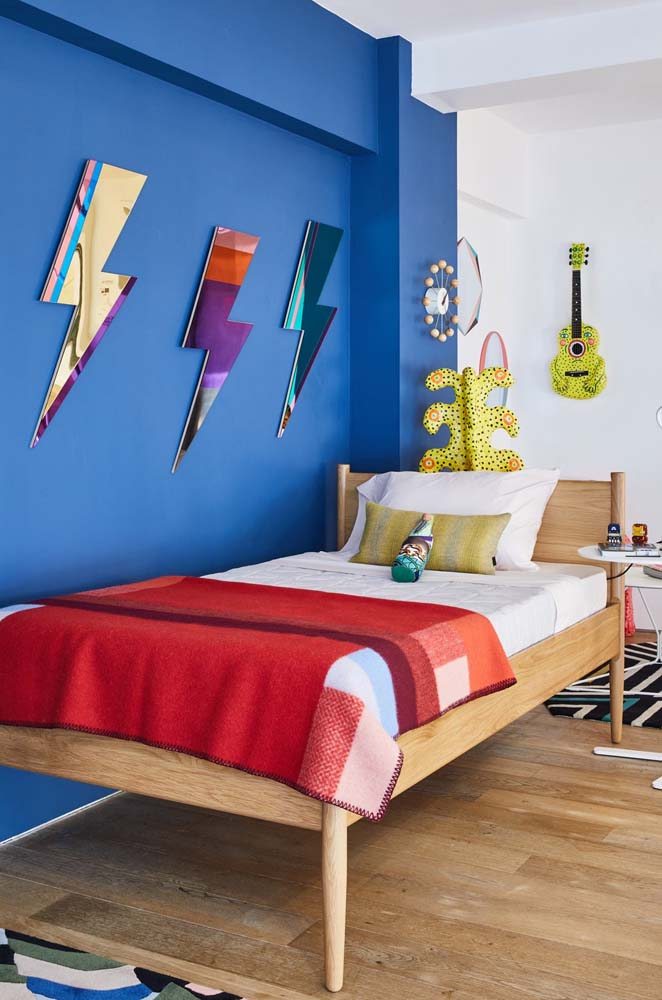 Quarto de adolescente com pintura azul e cama de madeira simples com cabeceira.