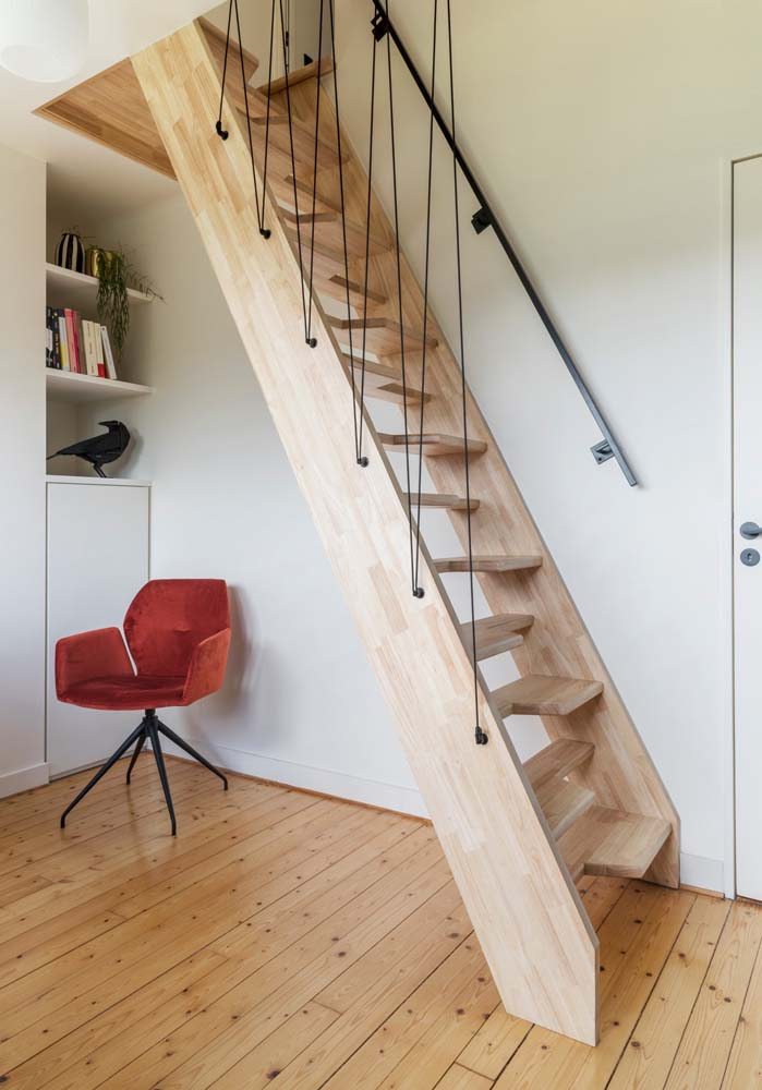 Escada inclinada com cabos suspensos de madeira clara e corrimão lateral para um ambiente bem compacto.