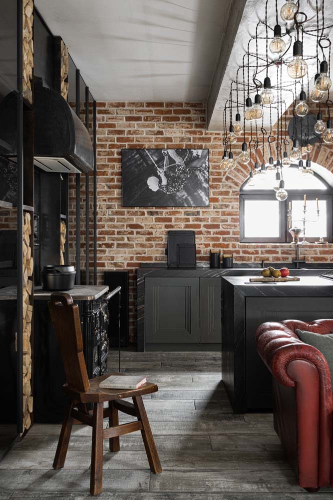 Piso marrom escuro e parede de tijolos nesta cozinha com armários planejados na cor preta.
