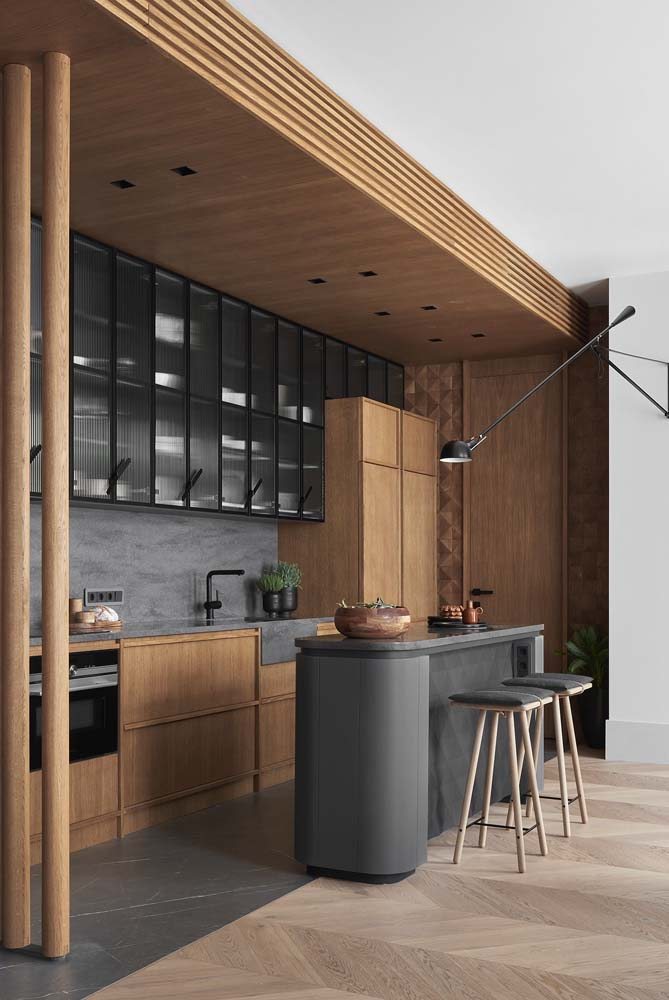Cozinha compacta e estreita com pequena bancada central na cor cinza escura e armários de cozinha planejado na cor marrom clara.