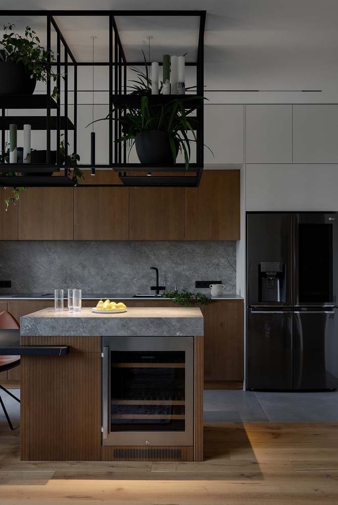 Lindíssimo projeto de cozinha moderna grande com armários na cor marrom e revestimento cinza na parede na altura da bancada.