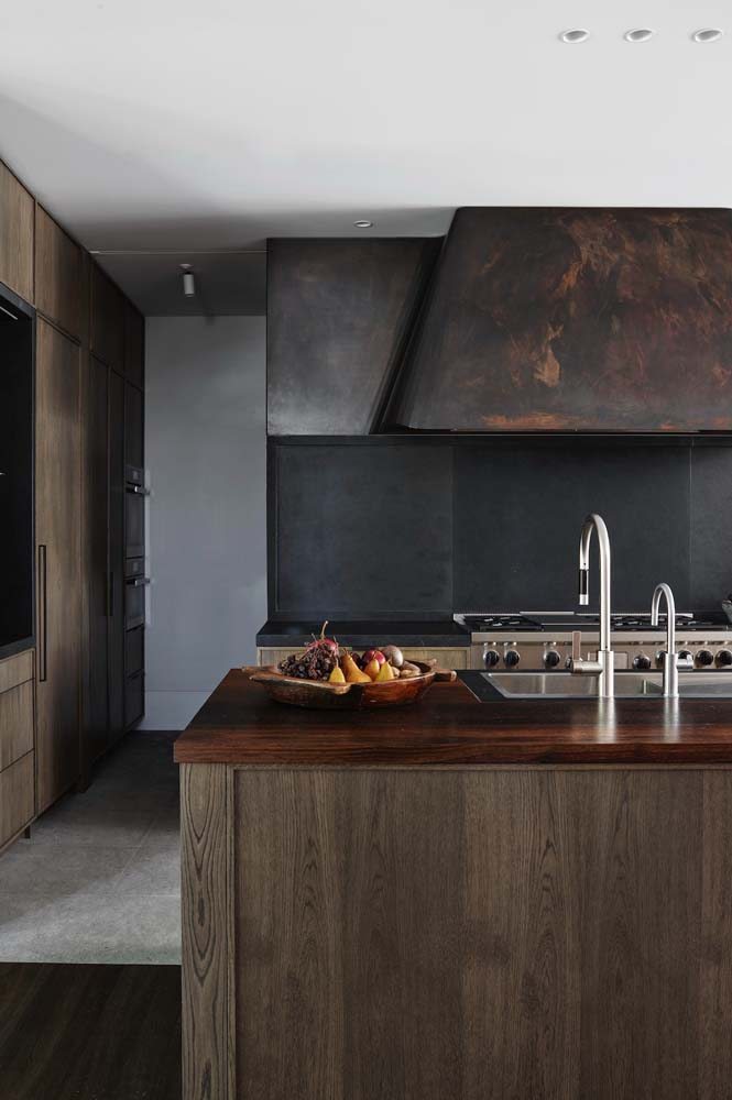 Modelo de cozinha americana planejada com armários com madeira marrom e bancada com revestimento preto.