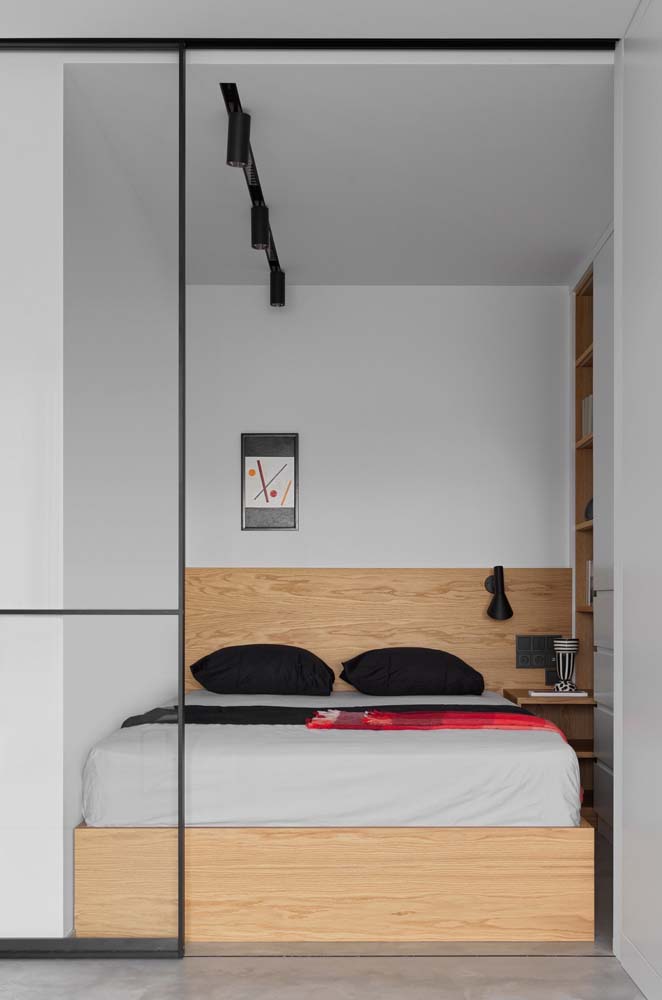 Quarto minimalista compacto com pintura cinza, cabeceira e cama de madeira clara.