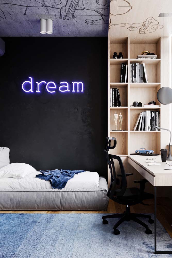 Lindo quarto de solteiro com cama cinza, carpete azul, parede estilo lousa com letreiro neon e escrivaninha com prateleira.