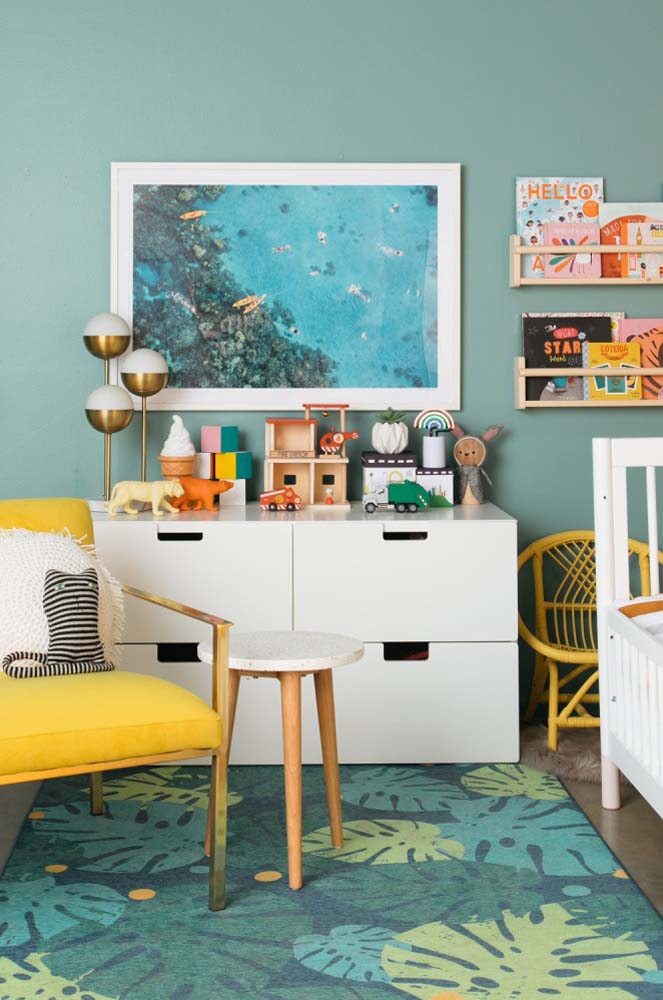 Criando um ambiente aconchegante: comoda infantil branca em meio a uma decoração de quarto infantil com verde água na pintura e itens coloridos.