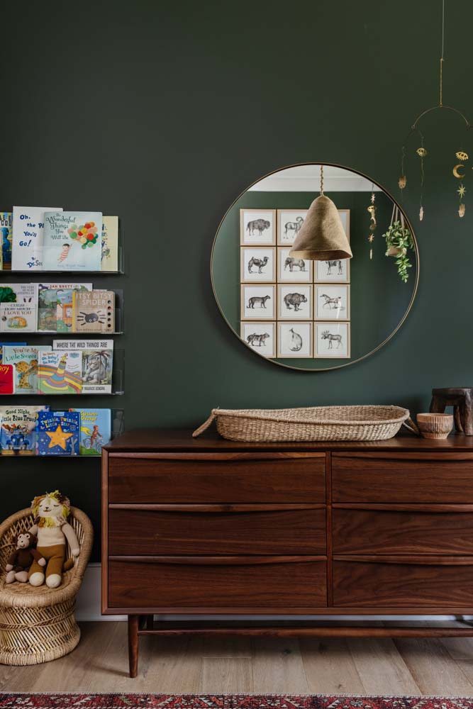 Ambiente intimista com pintura verde na parede, cômoda na cor madeira escura e prateleira para livros.